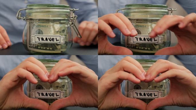 女性的双手在装满美元、美元、现金、纸币的玻璃罐前展示着爱心的标志，上面写着“旅行”。准备省钱。适度消