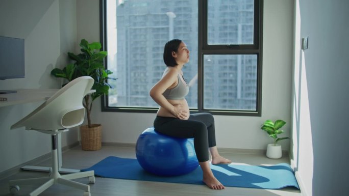 孕妇坐在家里的健身球上做骨盆底旋转