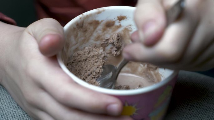 慢镜头中，小孩用勺子从纸杯里舀起巧克力冰淇淋