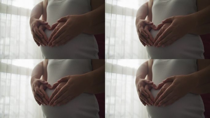 一对情侣手放在怀孕的肚子上，摆出心形
