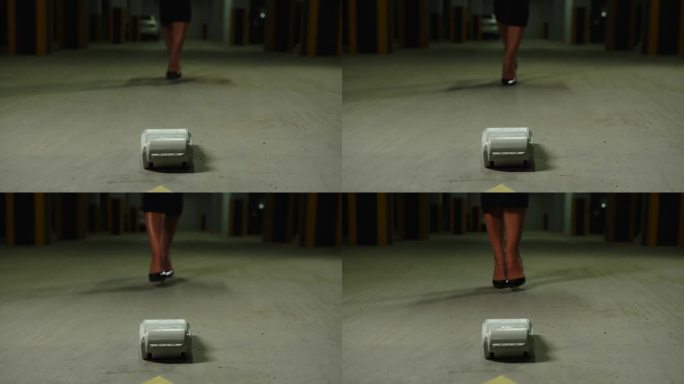 地下停车场里穿着高跟鞋的女性腿特写。女人走近躺在地上的收银机