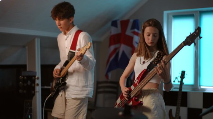 两个青少年在一所现代音乐学校弹电吉他。一个年轻人手里拿着拨片在弹电吉他，一个女孩在弹贝斯吉他。