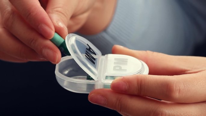 妇女用手将药片和营养补充品放入药片收纳器或塑料药片盒中并合上。