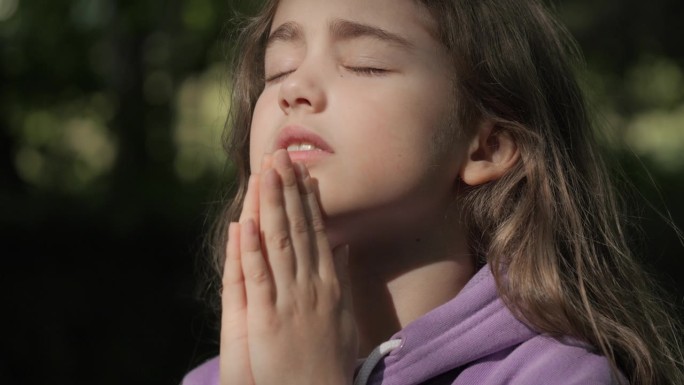 宗教。小女孩双手合十祈祷在户外向上帝祈祷。忧心忡忡的少女在寻找希望和信仰，向上帝祈祷。笃信宗教的孩子
