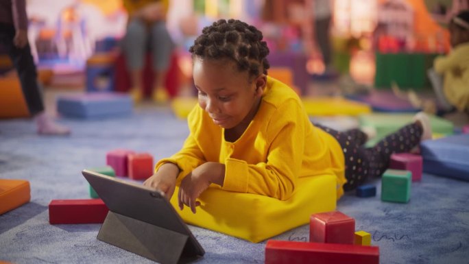 一个可爱的时尚黑人女孩使用平板电脑学习新技能和交流的肖像。快乐的非洲孩子在学前班度过了富有成效的时光