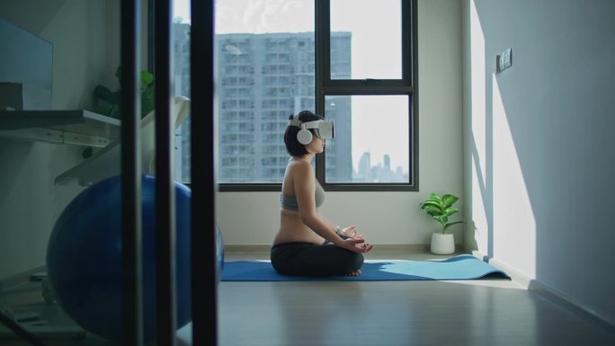亚洲成年孕妇戴着VR虚拟眼镜放松地坐在家里的客厅里，一边冥想一边做呼吸练习