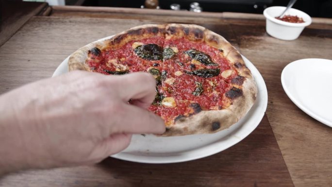 在亚利桑那州凤凰城的比安科披萨店里，盘子里放着煮熟的番茄酱披萨，一只手拿起一片，视频很稳定。