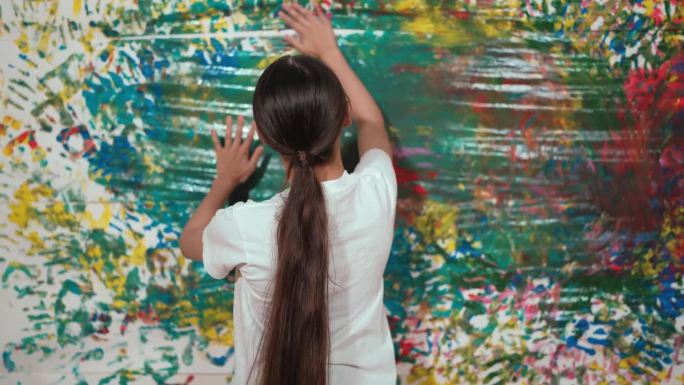可爱女孩的后视图，用彩色的手涂满了污迹斑斑的墙壁。启迪