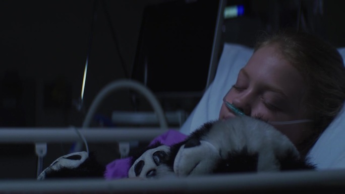 小女孩抱着她的玩具熊躺在医院的病床上睡觉