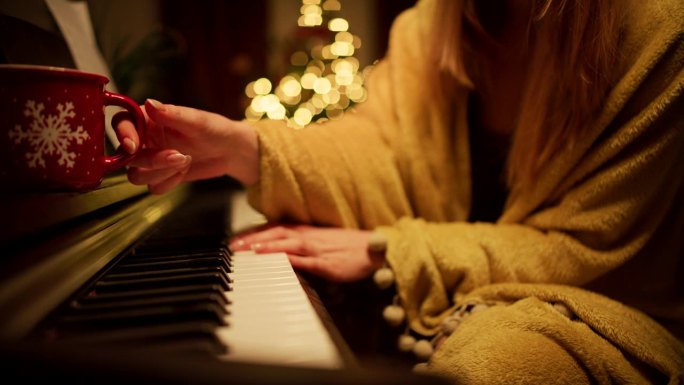 一个裹着毯子的女人在一棵挂满灯的圣诞树的背景下弹奏着圣诞颂歌。