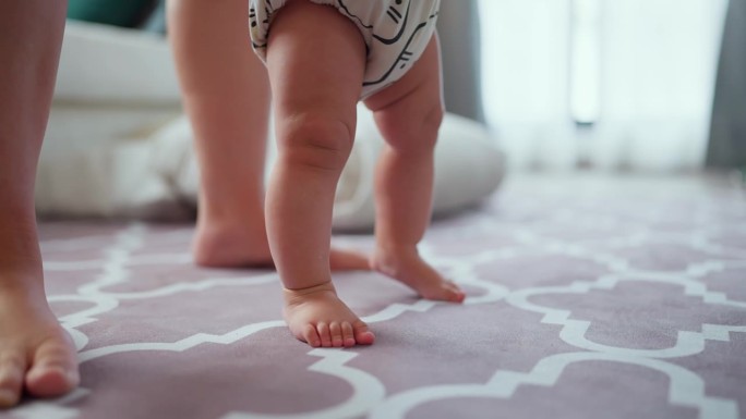 婴儿的第一步一个赤脚婴儿的腿在客厅里走路的慢动作，就在一个男婴迈出第一步的手持镜头后面
