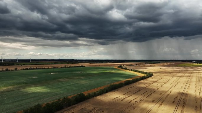 漆黑的天空和大片的雨云笼罩着田野。远处下着大雨。沿着耕地飞行。