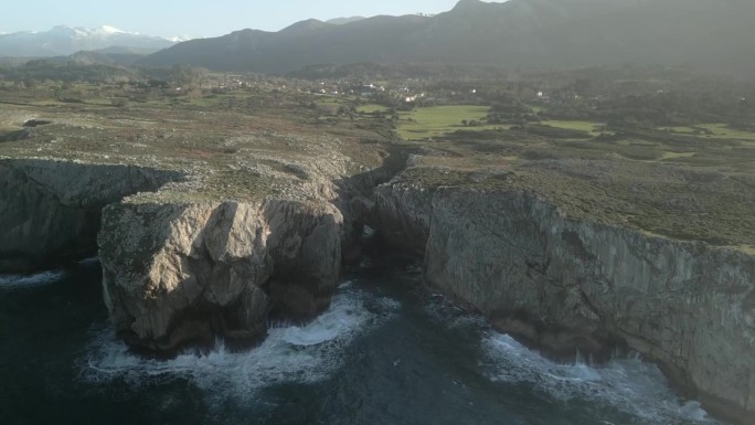 海中的一些悬崖的鸟瞰图，蓝绿色的海水与岩石碰撞，还有山后面的一些草地