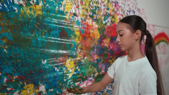 年轻的女孩拿着彩绘托盘和彩绘墙。启迪