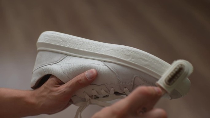 俯视图，男性用刷子和液体肥皂洗白鞋的脏鞋底。年轻人在家里擦拭运动鞋上的污垢和灰尘。