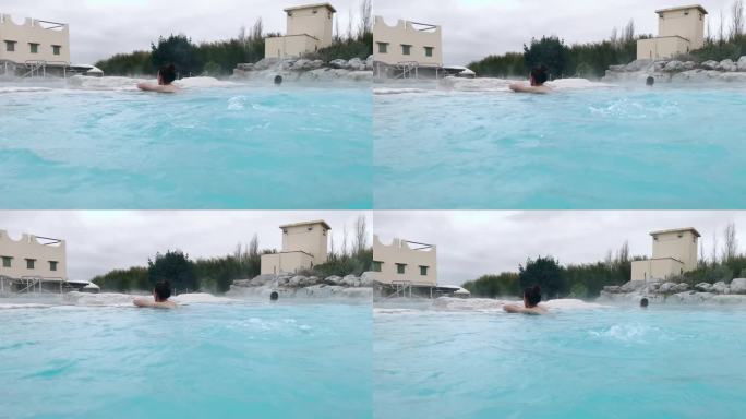 女子倚在池石上泡在温热的热水中，由于天然泉水含硫浓度高，水面有气泡，蓝色的热热水具有治疗功效，对人体