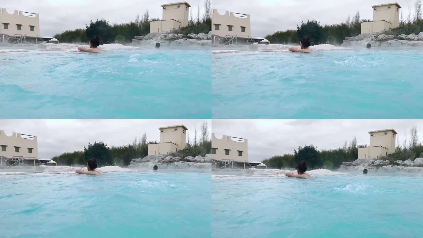 女子倚在池石上泡在温热的热水中，由于天然泉水含硫浓度高，水面有气泡，蓝色的热热水具有治疗功效，对人体