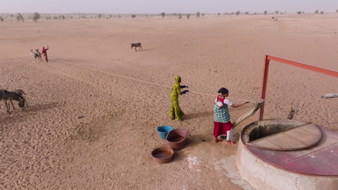 空中特写。在贫瘠的塞内加尔撒哈拉沙漠萨赫勒地区，三个黑人妇女在驴子的帮助下从一口深井里打水。干旱，气