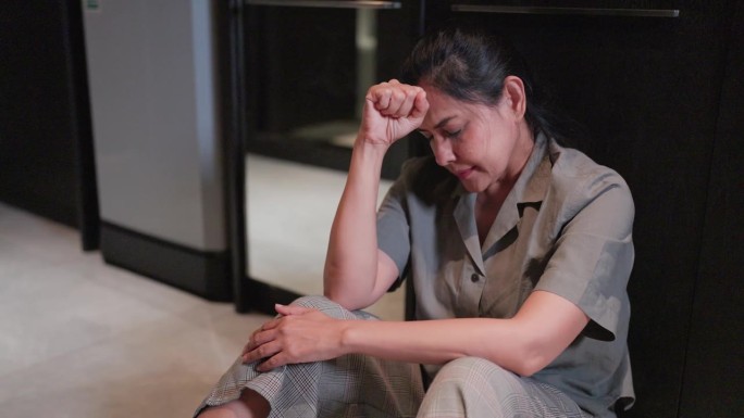 一个悲伤的女人坐在公寓的地板上，用手捂着额头。
