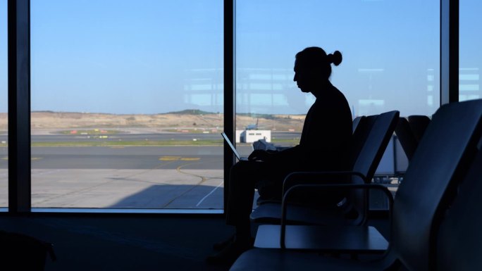 一名男子拿着笔记本电脑坐在机场休息室休息，看着窗外