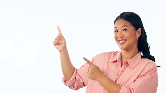 快乐的亚洲女人，指着广告名单在营销信息与工作室背景。女性的肖像微笑显示通知，好交易或销售折扣的实体空