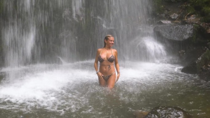 一个女孩在山间湖泊的瀑布下洗澡。
