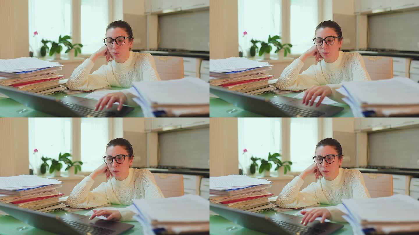 戴眼镜的女人在家里用笔记本电脑工作，桌子上散落着文件