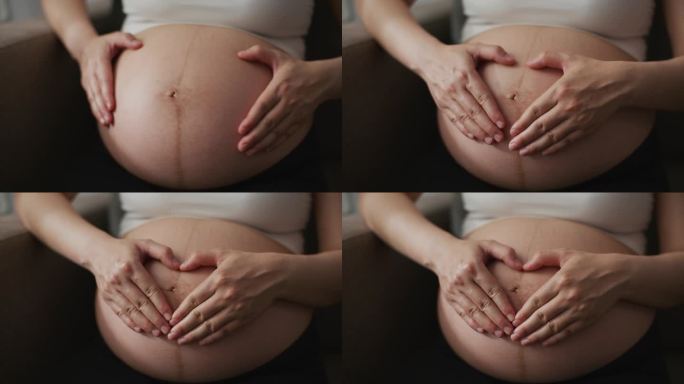 特写镜头:孕妇在赤裸的肚子上制作心形手