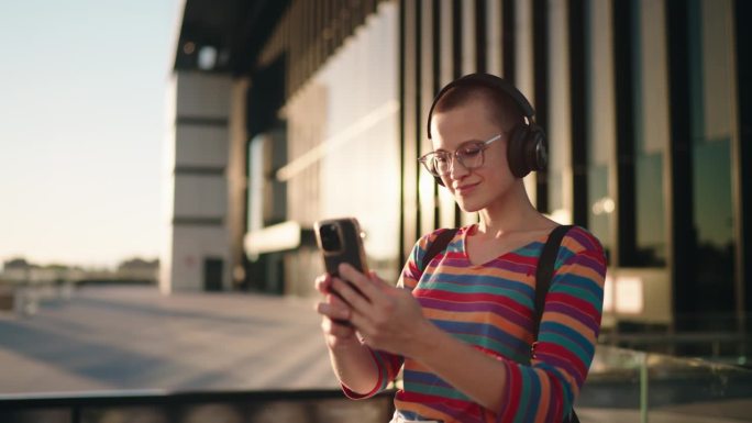 戴着眼镜和耳机的微笑女子在城市环境中用智能手机进行视频通话，这是在数字世界中保持联系的概念