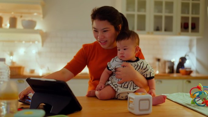 亚洲家庭关系纽带母亲视频电话会议在家里与婴儿工作多任务妈妈抱着男婴在厨房