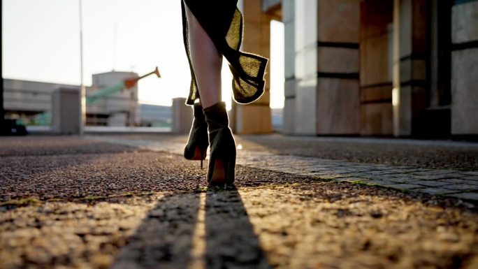 时尚走秀，城市里一个人穿着高跟鞋在大街上进行造型，时髦又别致。夏天，阳光和地面上的模特穿着时髦的鞋子