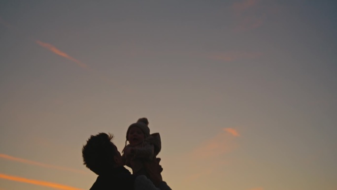 照片中父亲与儿子的深情时刻:黄昏时分，父亲张开双臂，将他心爱的孩子高高举起