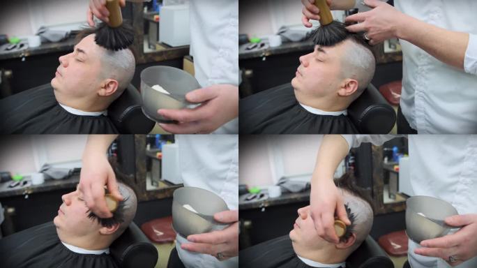 理发师在用直刀剃须之前，先用刷子在顾客头上涂上泡沫
