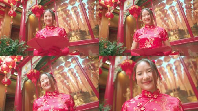 年轻的亚洲女孩穿着红色旗袍，在中国寺庙里拿着红包，向空中扔红包。给父母礼物或钱。