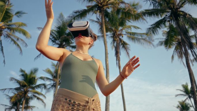 年轻女子探索虚拟环境，在棕榈树中戴着VR耳机。交互技术仿真，用户手势在身临其境的数字世界。女性参与增