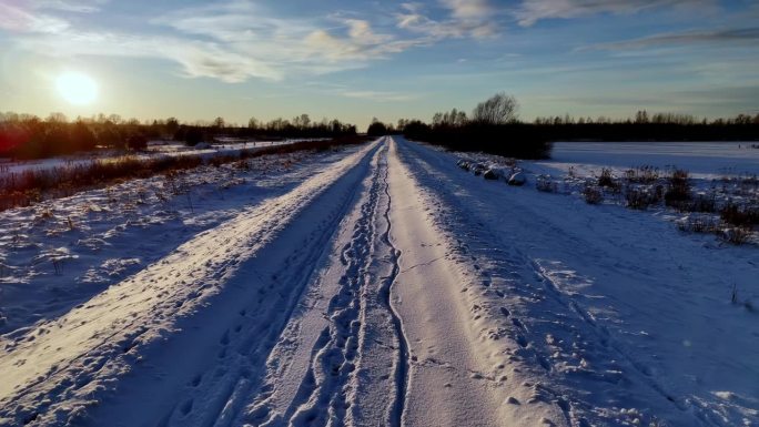 白雪覆盖的道路一直延伸到远处，天空湛蓝，夕阳投下长长的影子