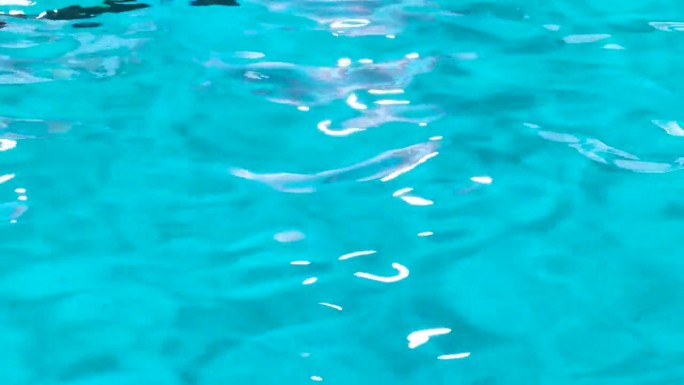 游泳池里的水在阳光的反射下荡起涟漪。泳池水面图案的背景照片。波纹和清澈的绿松石水面纹理
