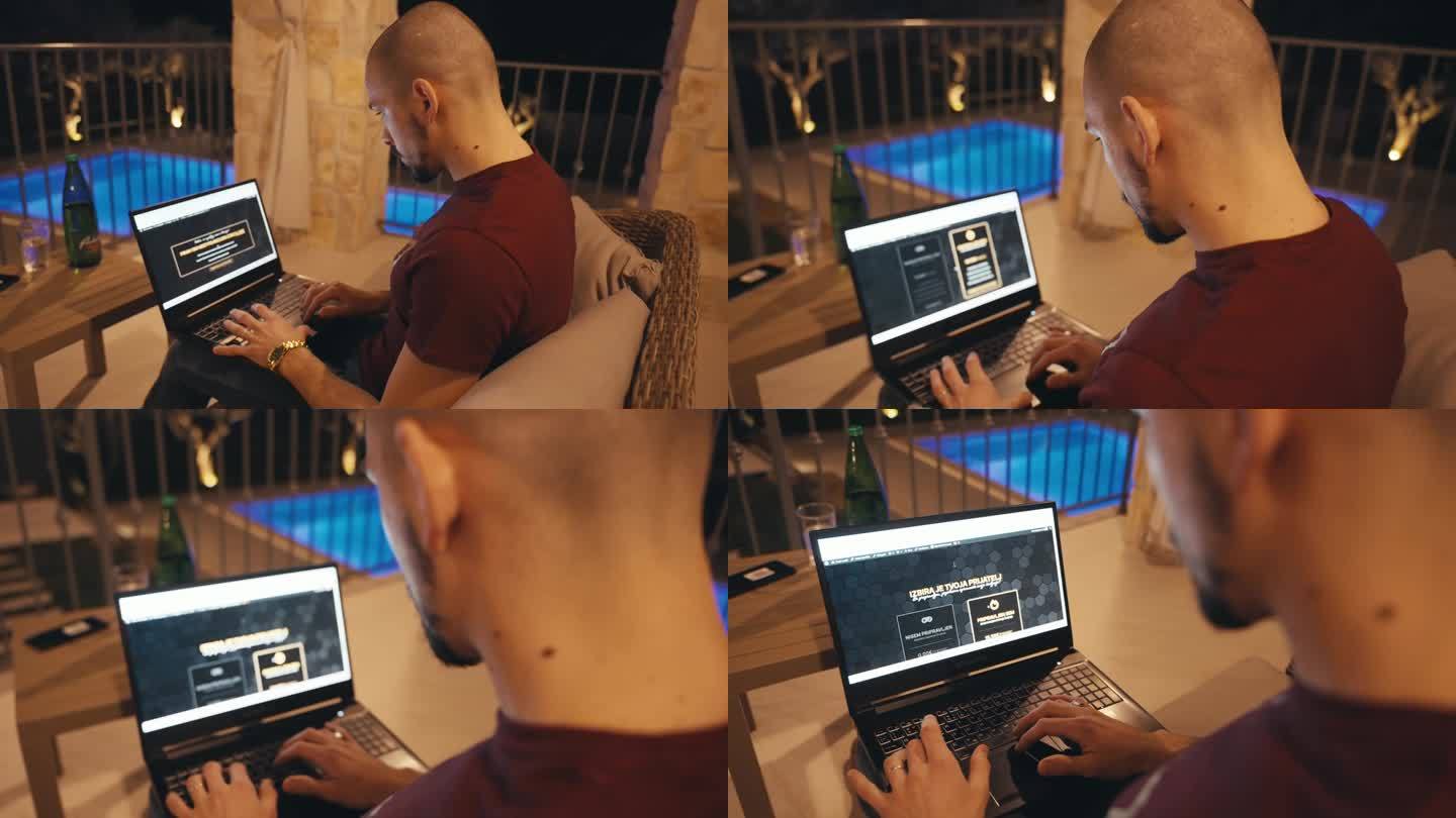 秃顶的年轻自由职业者晚上坐在别墅阳台上用笔记本电脑工作