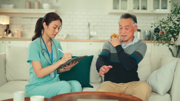 年轻的亚洲女性专业护士看护者检查肌肉和关节骨骼肩部疼痛个人护理护士帮助老年病人男性谈话谈话在家里的沙