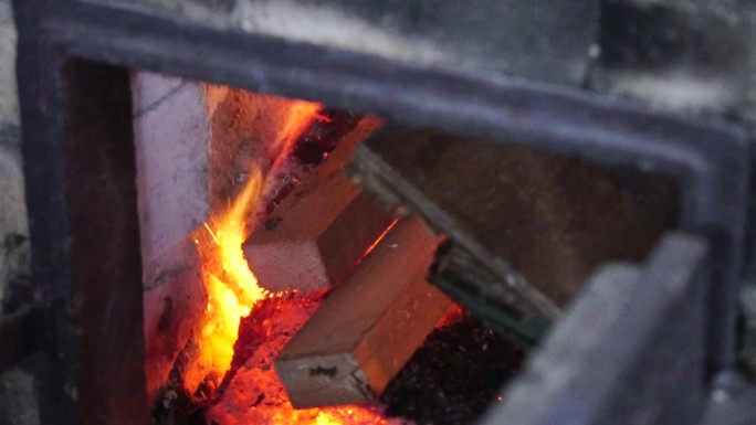 在采暖季节使用石炭炉进行木质家庭供暖。把圆木放到烧木头的炉子上的人。慢动作