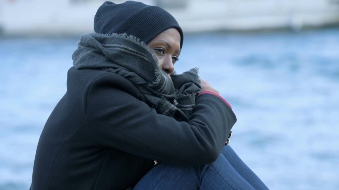 年轻忧郁的黑人女子在寒冷的日子里坐在码头上忧郁得像湖水