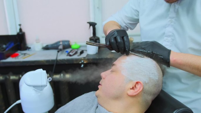 理发师在汽化器喷出的热气流下给一个男人剃头。