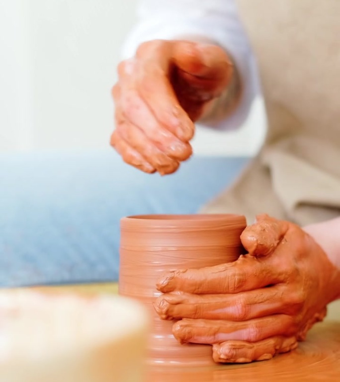 一位妇女的手在用陶轮制作杯子
