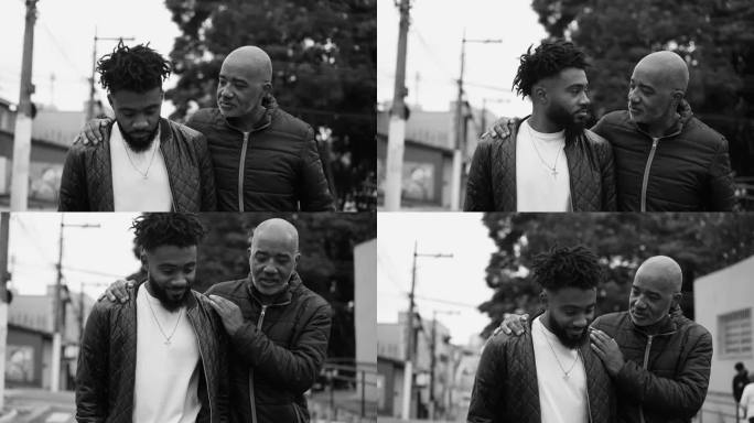 父亲和儿子谈话——中年的非裔美国父亲指导成年的儿子挽着手漫步在黑白单色的城市街道上