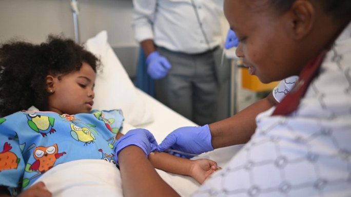 友好的非洲护士在病房的病床上给可爱的女孩手臂上打点滴，与她击掌