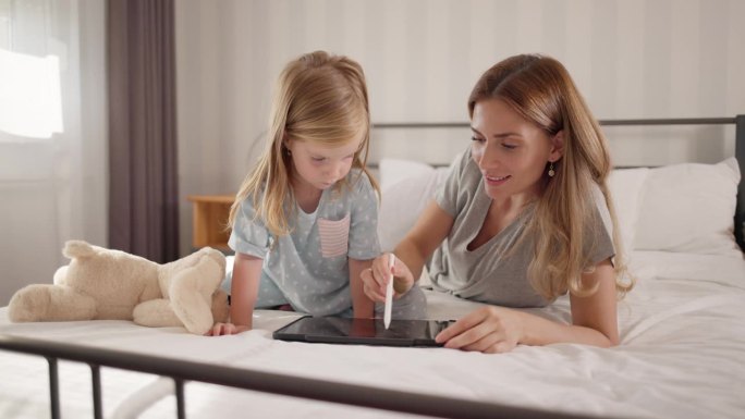 母亲和一个可爱的女孩子在卧室里的数码平板电脑上涂色