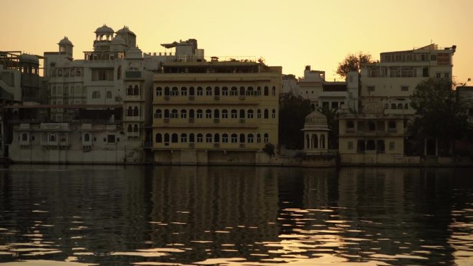 当太阳在印度乌代普尔的皮丘拉湖下下沉时，优雅的鸭子在水面上滑行，与令人惊叹的建筑的宁静背景相辅相成，