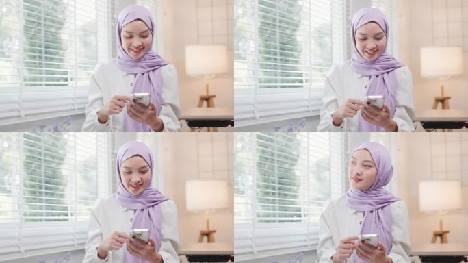 美丽的年轻亚洲穆斯林妇女在客厅使用智能手机的肖像