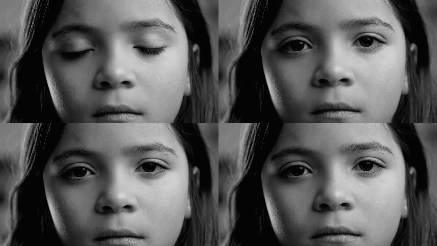 严肃的小女孩的特写脸盯着相机在黑白，单色。宏观肖像带有庄重悲伤的沉思表情