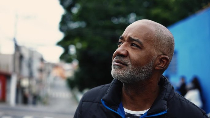 沉思的50多岁的非洲裔美国人，在街上散步时观察城市周围的环境，一个黑人中年人的特写脸部跟踪镜头，沉思